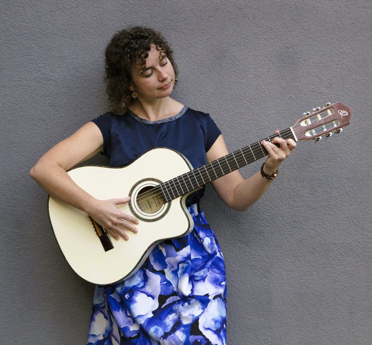 Ilva spielt Gitarre beim Mantra-Singen – ruhiger, konzentrierter Moment mit akustischer Gitarre vor neutralem Hintergrund.